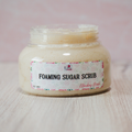 Jar of foaming sugar scrub with a label on a light wooden surface