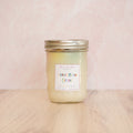 White candle in a jar labeled 'Saturday Morning Cartoons' on a white surface.