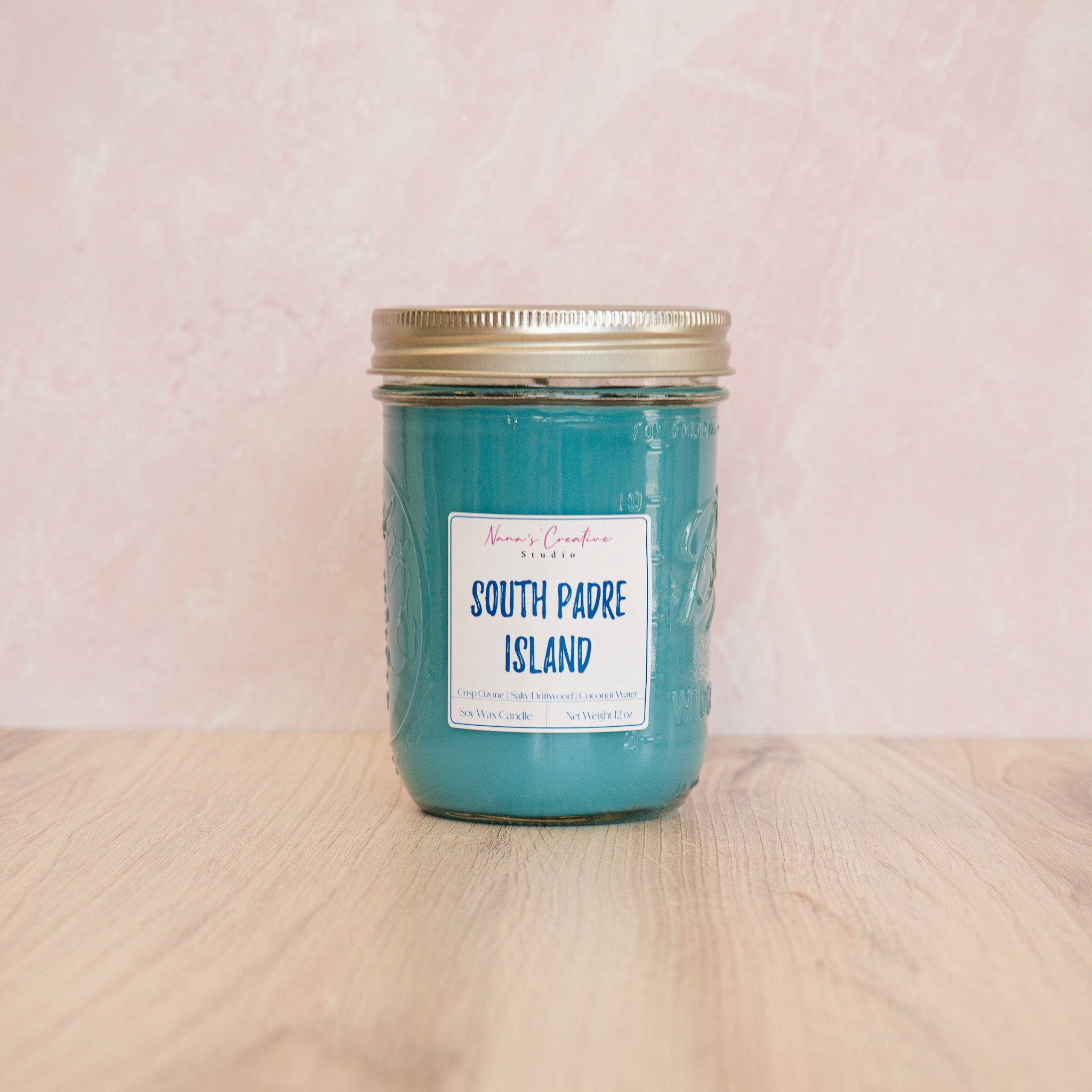 Blue candle in a jar labeled 'South Padre Island' on a white surface.